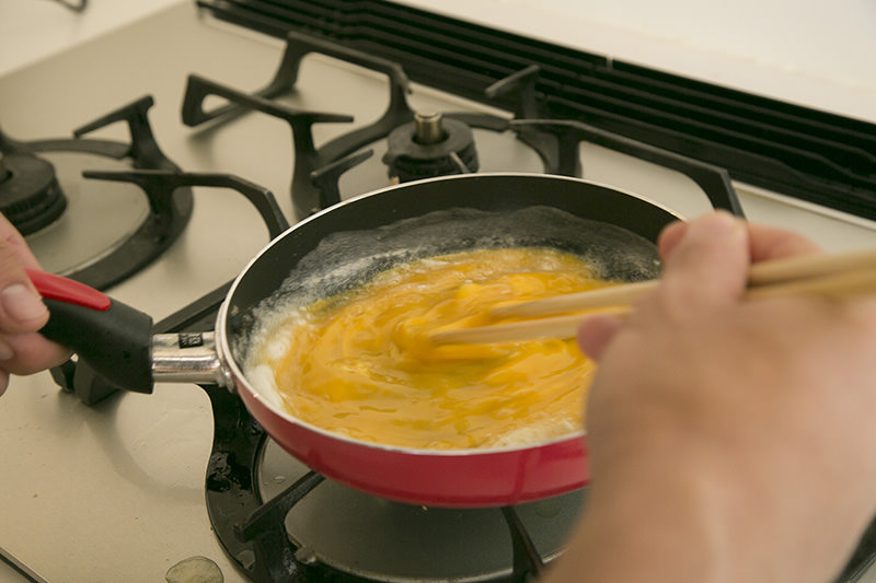 フライパンを振りながら、菜箸で卵を激しくかき混ぜ