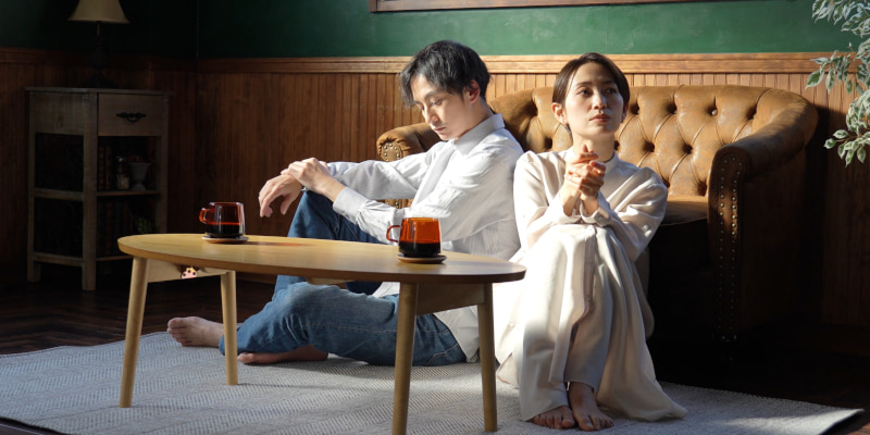 暗い表情で違う方法を向いてリビングの床に座るカップルの写真