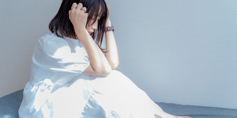 頭を抱えて座っている白ワンピースの女性の写真