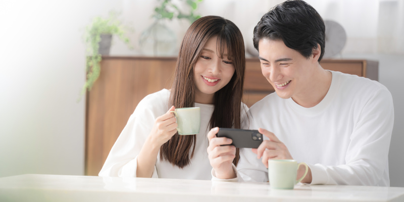 家で楽しそうにスマホを見ているカップルの写真
