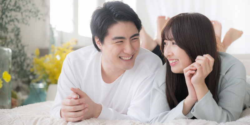ベッドに寝転がって楽しそうにしゃべる男女の写真