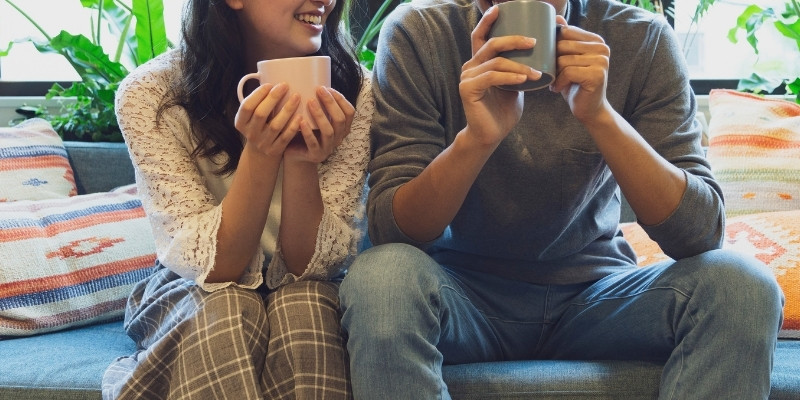 ソファに腰かけてマグカップを持っているカップルの写真
