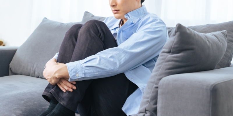 ソファで膝を抱えて座る男性の写真