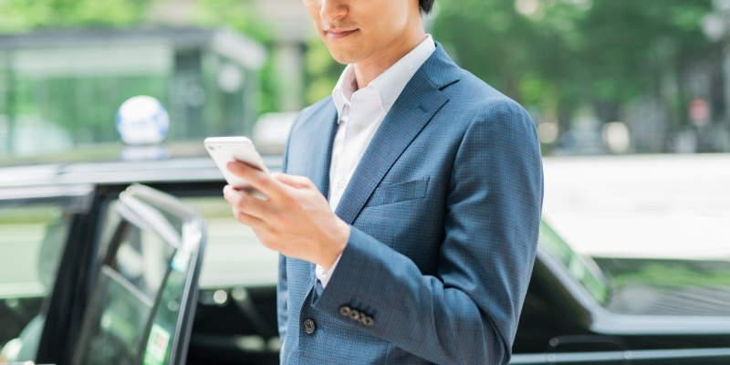 タクシーから降りてスマホを見ている若いビジネスマンの写真