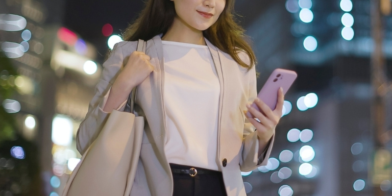 帰りの夜道でスマホを見ているビジネスウーマンの写真