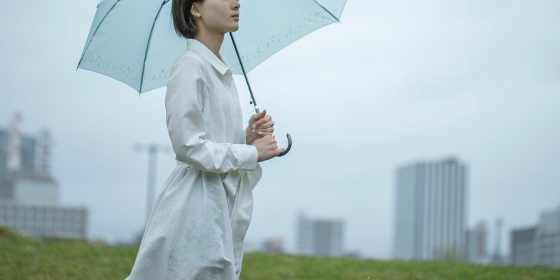 傘を差した白いワンピースの女性が佇んでいる写真