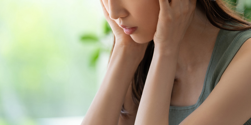 両手で頭を押さえてうつむき、どうしようと考えている女性の写真