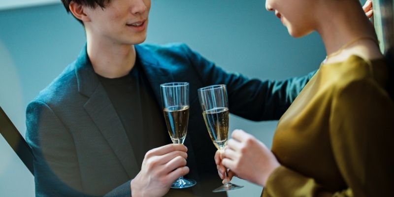 グラスを持った男女二人の写真。男性が壁ドンの姿勢で女性を口説いている