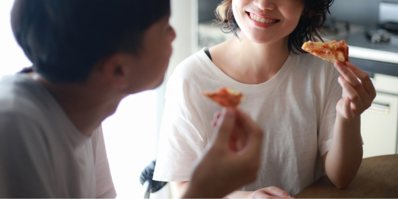 笑顔でピザを食べている男女の写真