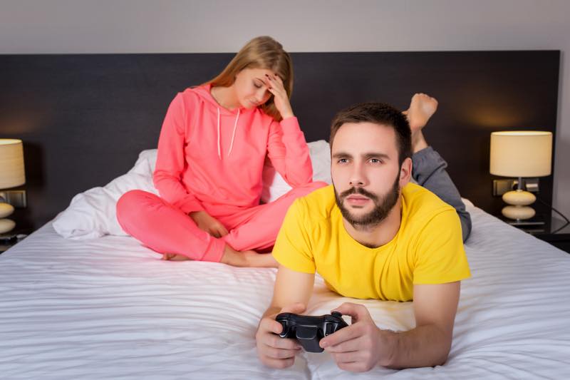 ベッドの上で悩む女性、ゲームする男性