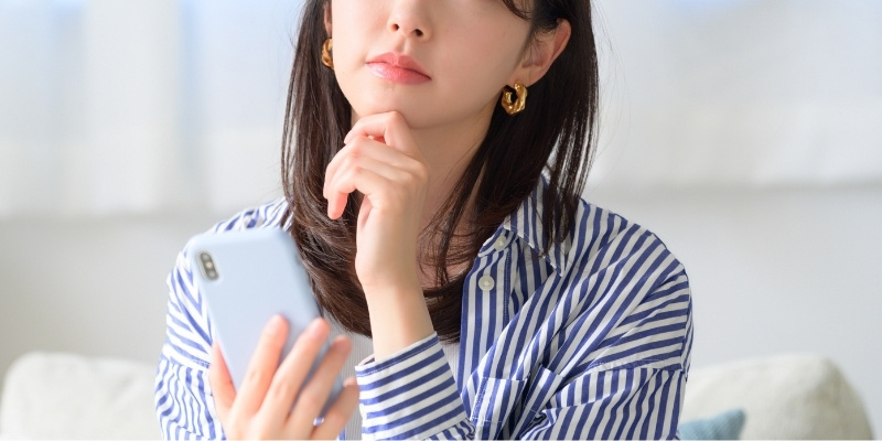 スマホを片手に考え込む女性の写真