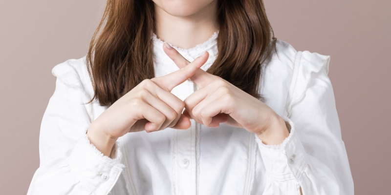 指でNGポーズを作る女性の写真