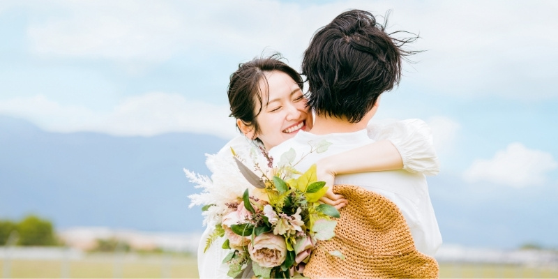 野原で抱き合う花束を持った新郎新婦の写真