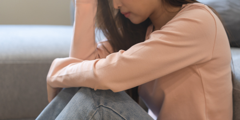部屋に座って頭を抱えながら悩む女性の写真