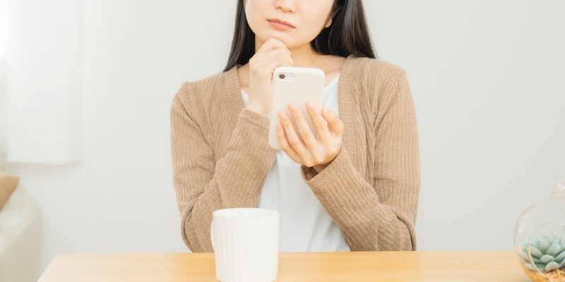 スマホを片手に考える女性の写真