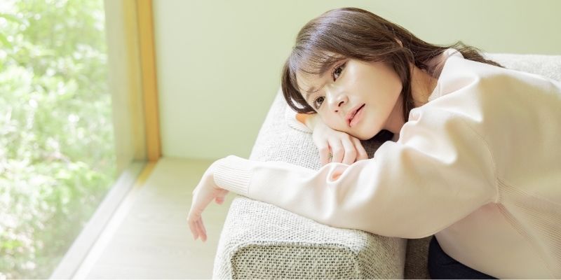 枕にもたれかかって寝ころぶ女性の写真