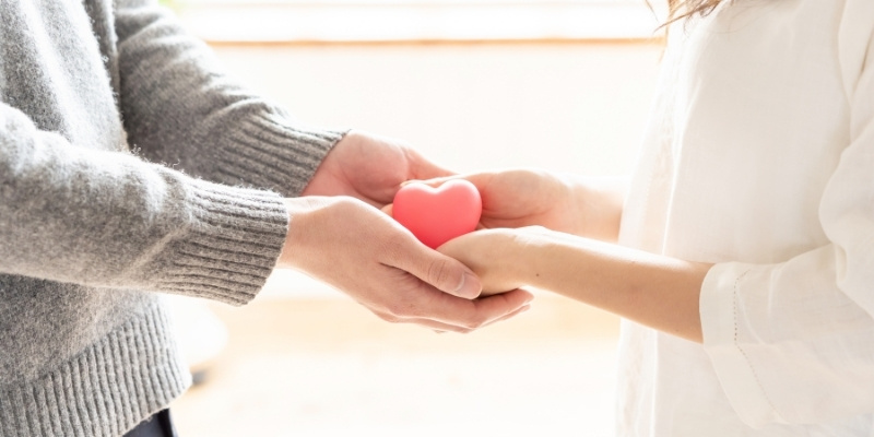 ハートのオブジェを両手で握りあう男女の手元の写真