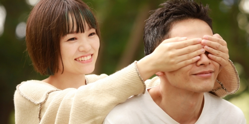 女性が手で目隠しをしているカップルの写真
