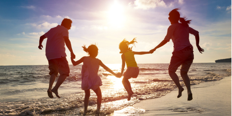 太陽を背景に砂浜で飛び跳ねる親子4人