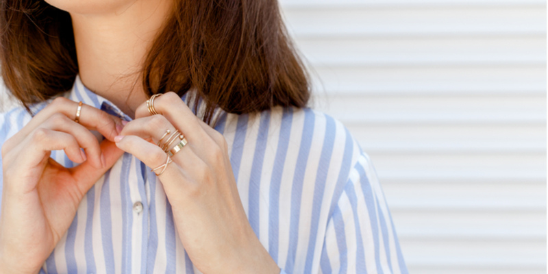 襟のボタンをとめる女性の左手薬指の指輪