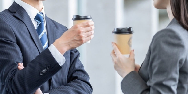 コーヒーを片手に会話するスーツ姿の男女の写真