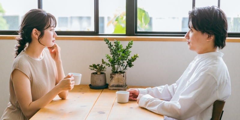 カフェで白けた表情をして向き合うカップルの写真