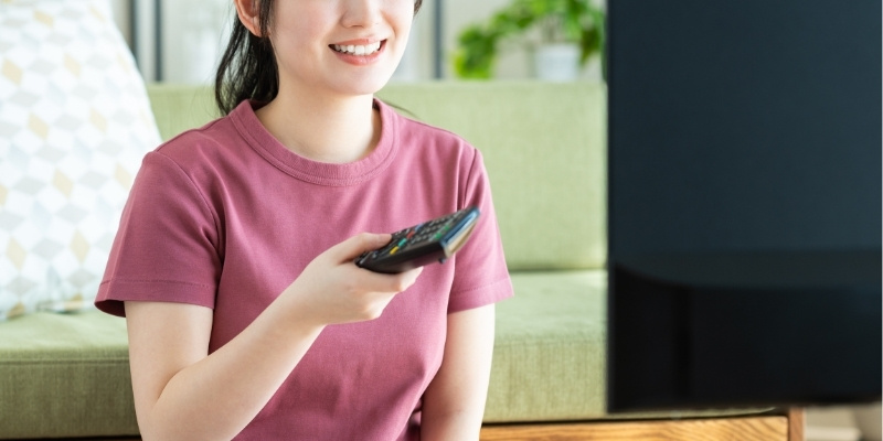 リモコンを手に持ってテレビを見ている女性の写真