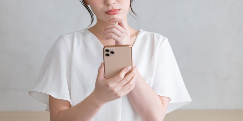 スマホを見ながら悩む女性の写真