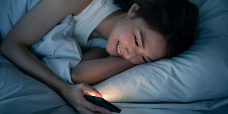 夜に布団の中でスマホを見ている女性
