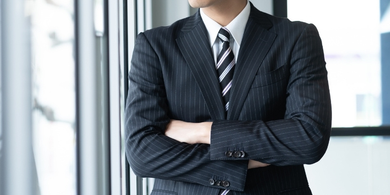 腕を組んで窓の外を見つめるビジネスマンの写真