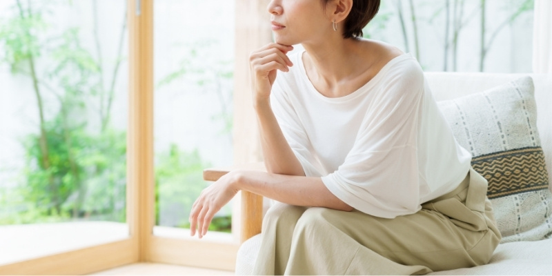 窓の外を眺めて考え事をする女性の写真