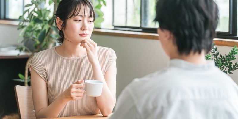 カフェにいるカップルの写真。彼女はコーヒーを片手に退屈そうな顔をしながら目をそらしている