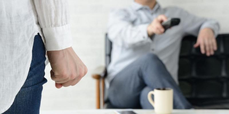 テレビのリモコンを持つ男性と、手前に握り拳を握った女性の手元