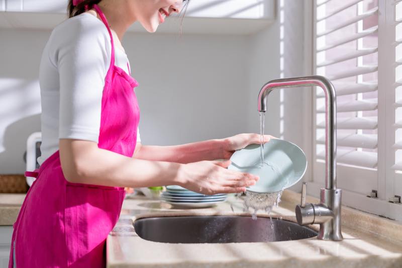ピンクのエプロンをつけた女性がお皿を洗っている