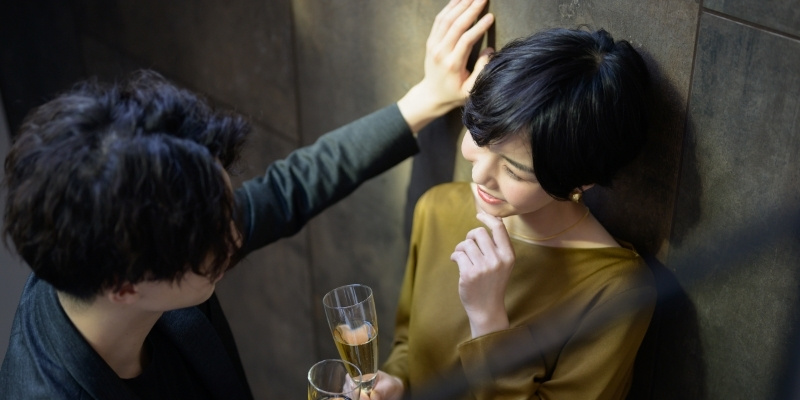 バーで男性に壁ドンされている笑顔の女性の写真
