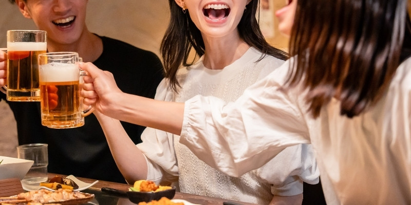 居酒屋にて生ビールで乾杯する男女3人の写真