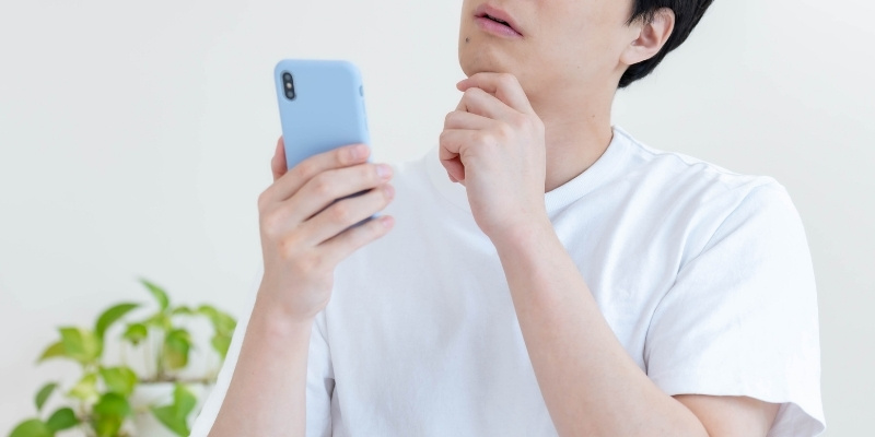 スマホを片手に考える男性の写真