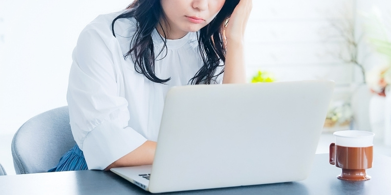 ノートパソコンの前で悩んでいる女性の写真