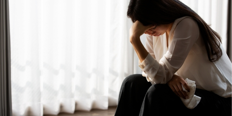 ベッドに腰かけて悩んでいる女性の写真