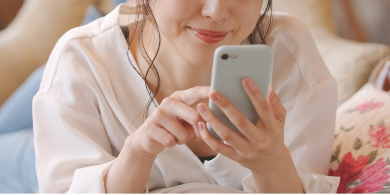 ベッドでスマホを操作する女性の写真