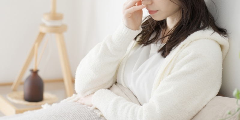 ベッドに座って悩む女性の写真