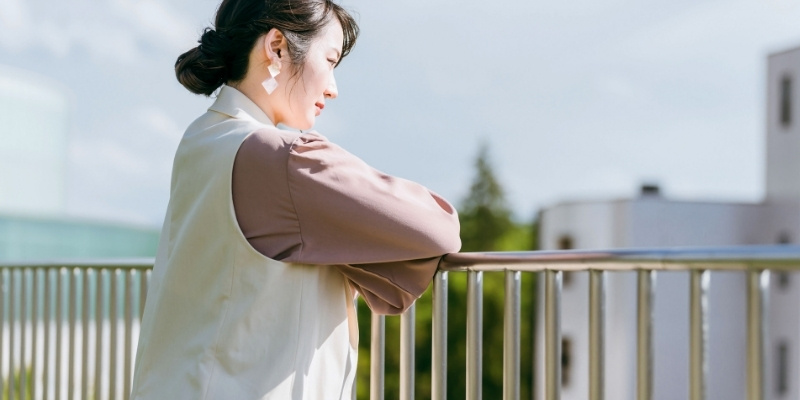 手すりに持たれて悩んでいる女性の写真