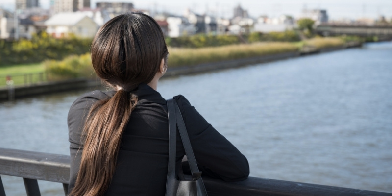 大きな川沿いの橋の欄干にたたずみ、上を見上げているビジネスウーマン