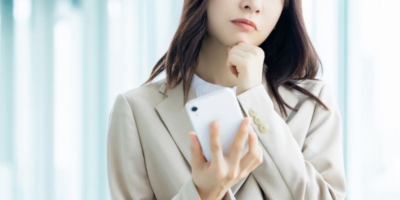 スマホを見て考え込むビジネスウーマンの写真