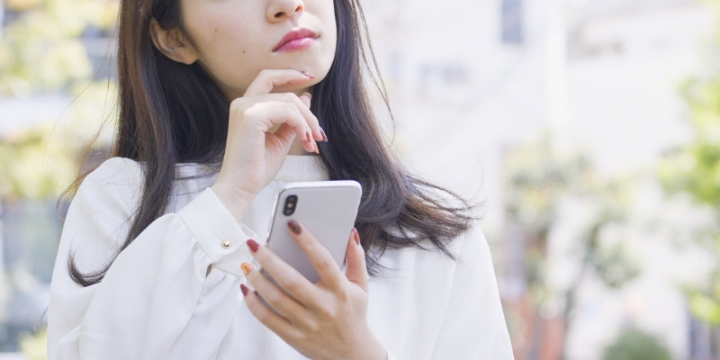 スマホを片手に考え込む女性の写真
