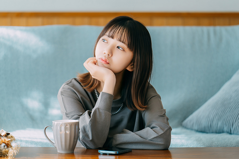 テーブルで頬杖をついて考え事をする女性