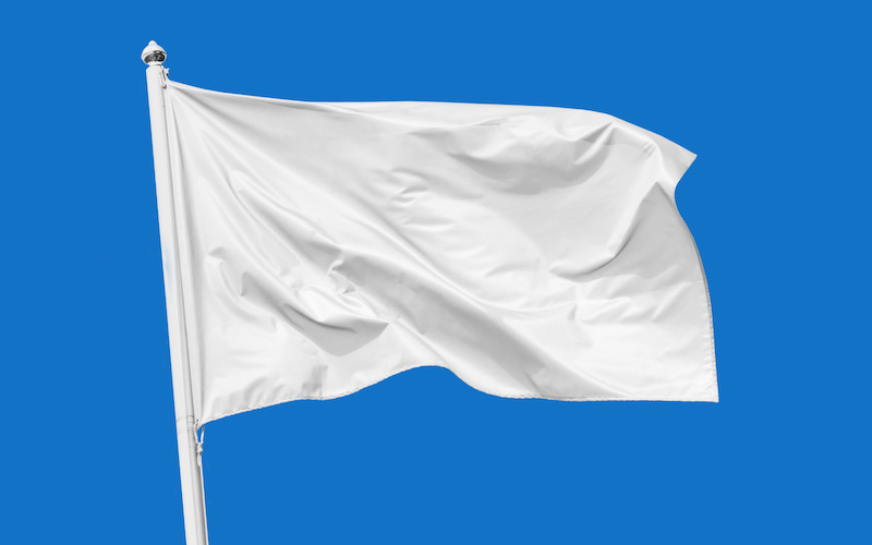 青空のもと掲げられた白い旗の写真