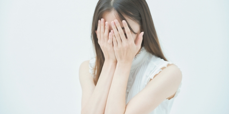 下を向いて顔を覆っている女性の写真