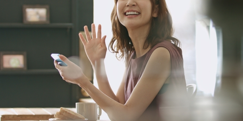 カフェで待ち合わせた相手に笑顔で手を振る女性の写真