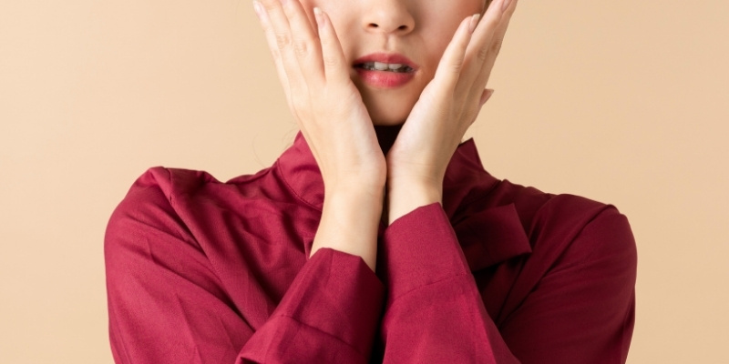 頬を両手で覆って困った顔をしている女性の写真